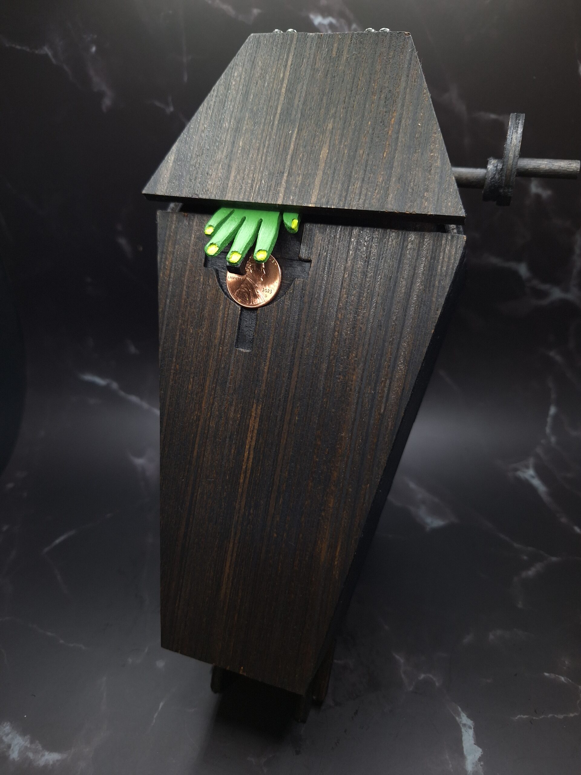 small black coffin with little green zombie hand reaching out for a coin